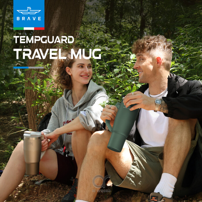 Two people seated in a wooded area, smiling and holding silver Brave Tumbler Mugs